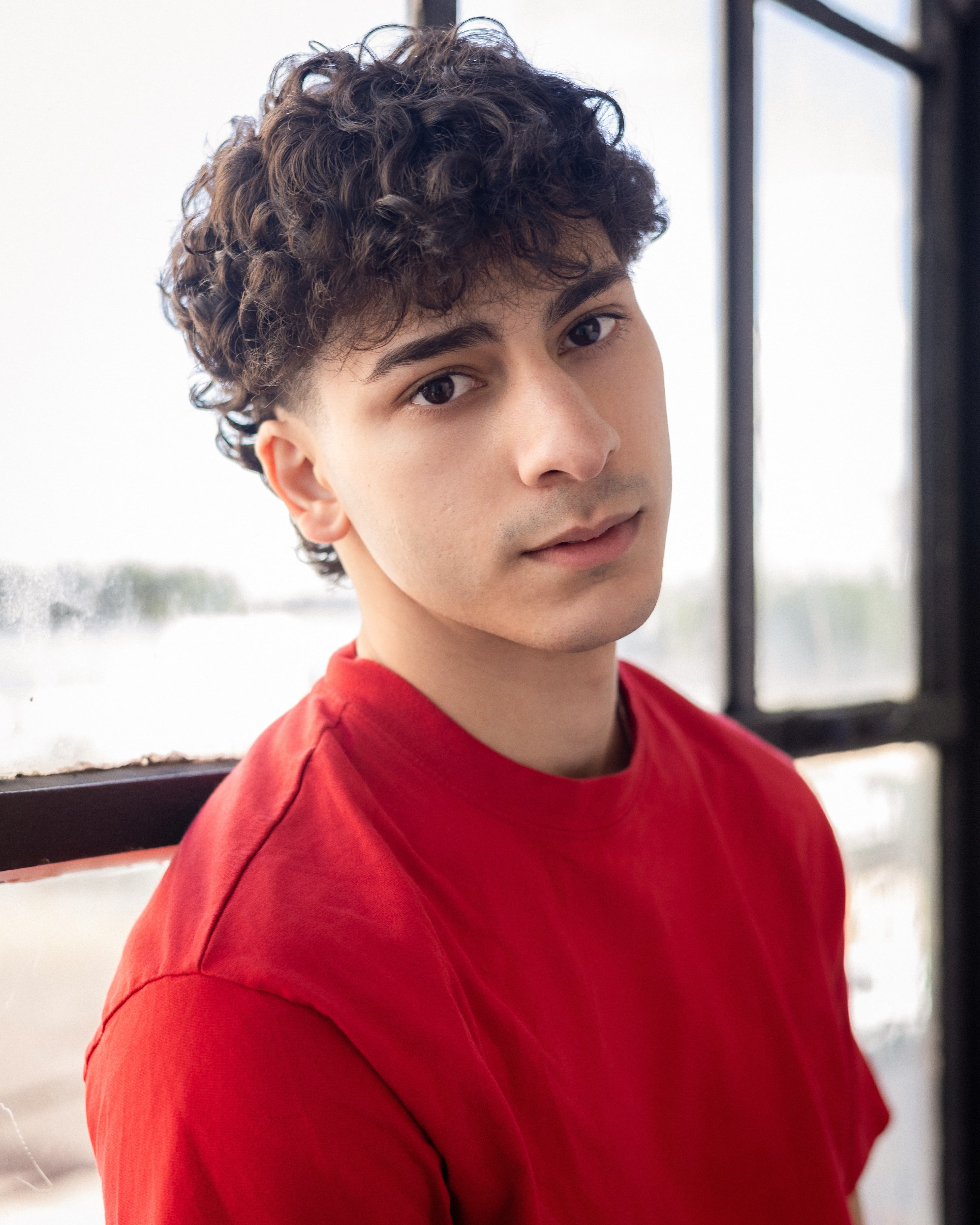 Adam in a red shirt beside a window
