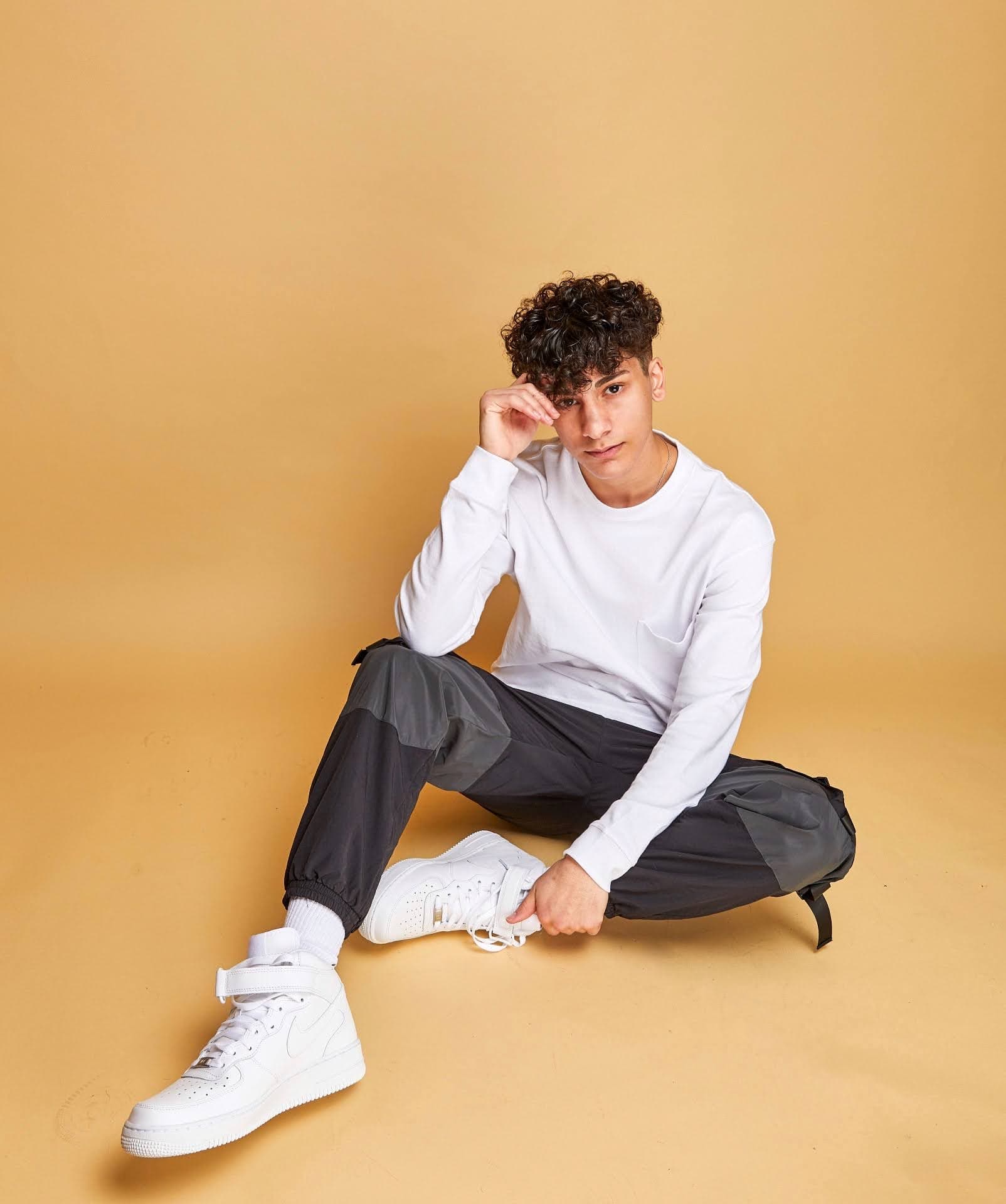 Seated full-body studio portrait of Adam against a golden background